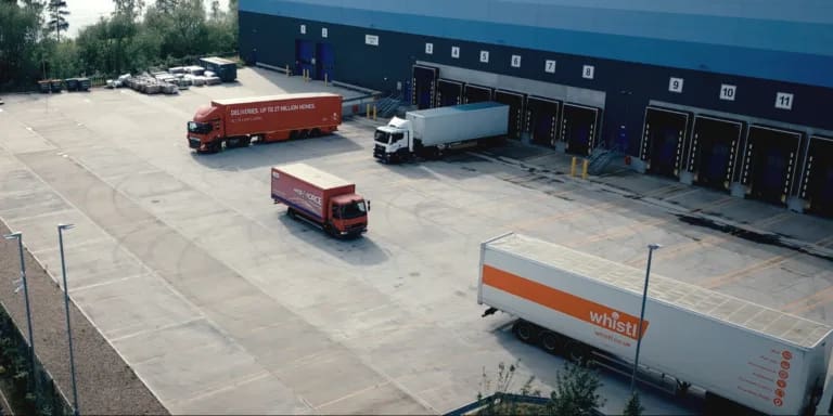 Fleet of lorries leaving modern 3PL warehouse under cloudy sky