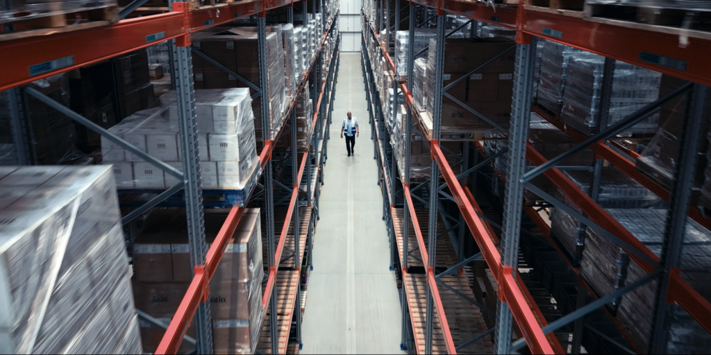 A member of staff strolls between two huge storage racks in a warehouse operated by a 3PL logistics services provider